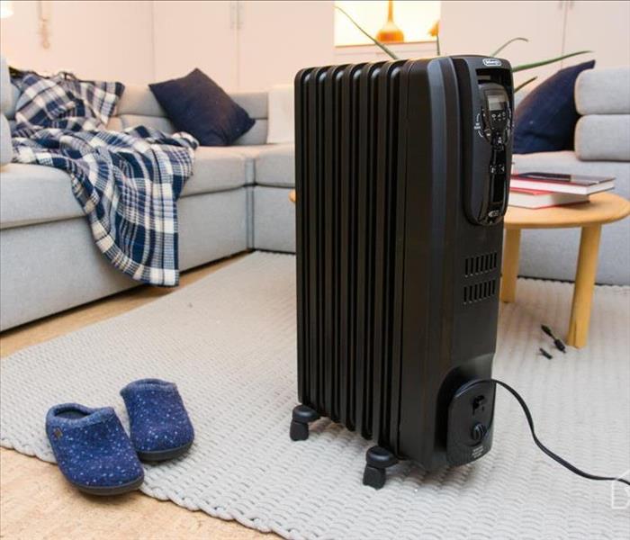 A Space heater sitting in the middle of the living room. There is a couch, slippers, and a coffee table sitting behind it. 